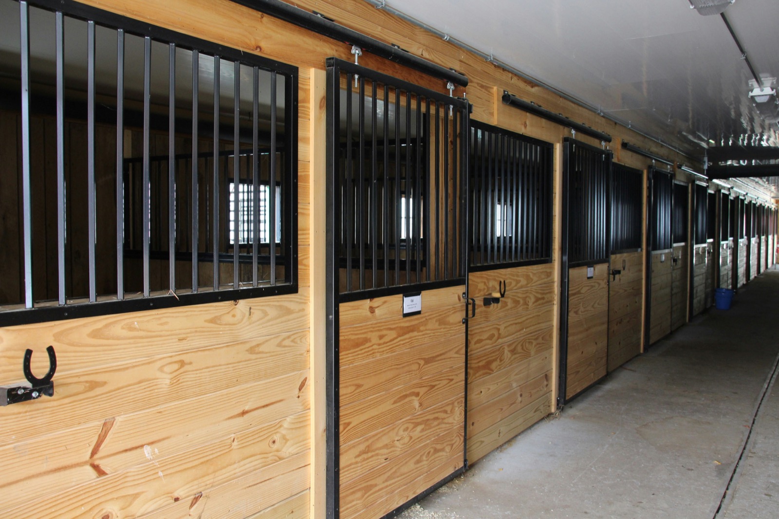 A bright, modern UK livery barn aisle with timber stable fronts and metal grilles — the kind of yard a careful listing makes findable.